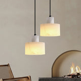 Pair of alabaster marble pendant lights casting a warm glow in a neutral-toned living room, placed above a fireplace with woven chairs in the foreground.
