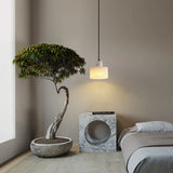 Alabaster marble pendant light installed beside a bed, illuminating a black side table with decorative accents in a calm, minimalist bedroom setting.