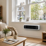 A white wall-mounted portable heater installed on a beige wall in a bright, modern living room with a wooden coffee table, sofa, and large windows.