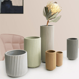 A collection of Carmarthen vases in various sizes displayed together. Vases feature vertical ribbed patterns in soft shades of green, grey, and tan, with a protea flower in the tallest vase.