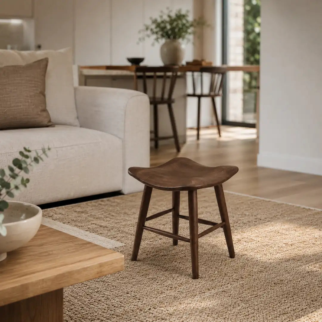 Wooden short stool styled in a cosy UK living room corner with soft lighting, neutral sofa, rug and shelving.