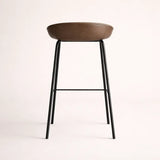 Bar stool with brown seat and black metal legs on a light pink background