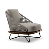  The chair features a knitted rattan frame, providing an intricate and elegant look. The seat and backrest are upholstered in a soft, grey fabric, offering comfort and a contemporary aesthetic. The chair has a wide, cushioned seat and a slightly reclined backrest for optimal relaxation. The base of the chair is made of dark wood, and it is supported by sturdy, angled metal legs in a black finish. 