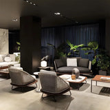 Elegant modern lounge area featuring stylish woven rattan chairs and a sleek dark sofa, complemented by lush green plants and contemporary decor, creating a cozy and sophisticated atmosphere