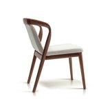 Side view of a mid-century walnut dining chair with a gracefully curved armrest and textured white seat cushion, displaying both style and comfort.