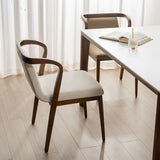 Contemporary dining room with a sleek white table and mid-century modern walnut chairs with textured light grey upholstery near sheer curtains.