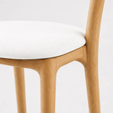 Close-up of oak wood bar stool frame with white upholstered seat and smooth designer leg detail