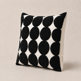 Three-quarter view of a black and white tufted cushion cover with raised polka dots and plain white cotton reverse, 45x45cm.