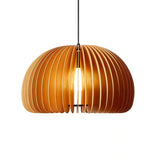 A close-up image of a modern wooden pendant light with a pumpkin-like design featuring curved, slatted panels in a warm golden hue. The light bulb at the center casts a soft, inviting glow through the slats, highlighting the elegant and organic shape of the lamp. The pendant is suspended from a sleek black cable, adding a contemporary touch to the natural aesthetic.