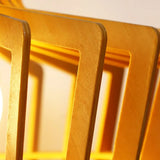 Extreme close-up of a wooden pendant light showcasing the detailed texture of its slatted panels. The golden yellow hue of the wood is enhanced by the warm light emanating from within, highlighting the fine craftsmanship and smooth finish of each individual slat. The image captures the interplay of light and shadow, emphasizing the depth and elegance of the wooden design.