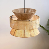 The lamp has a tiered design with three distinct sections: the top and bottom sections are made of a finely textured wood, while the middle section is crafted from golden rattan with an intricate, open-weave pattern. The warm light emanating from within casts a soft, inviting glow through the rattan, highlighting its detailed craftsmanship. 