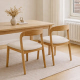 Dining table with two wooden chairs and white cushions in a bright room.