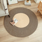 This image features a stylish two-tone round rug placed on a light hardwood floor. The rug showcases a natural beige center with a darker brown perimeter, arranged in a precise spiral pattern. A magazine and a white mug sit casually atop, suggesting a relaxed living space, with a snippet of an off-white sofa leg at the edge and a simple wooden side table in the background, enhancing the homey and modern aesthetic.