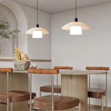 A chic and contemporary café setting featuring sleek wooden bar stools with round, brown leather seats and matching wood armrests. Overhead, simple pendant lights with a soft, white glow illuminate the minimalistic space, enhancing the modern aesthetic.