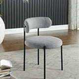 Contemporary dining chair in a cozy gray textured fabric, featuring a rounded seat and a minimalist black metal frame, placed in a modern living space with wood flooring.