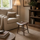 Wooden short stool in a bright UK living room beside a neutral armchair and round wood coffee table on a textured rug.