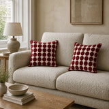 Two square throw pillows with a dark red and cream polka dot pattern displayed on a textured beige sofa in a cozy living room setting.