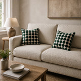 Two square throw pillows with a dark green and cream polka dot pattern styled on a light beige textured sofa in a cozy living room setting.