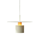 A contemporary pendant light featuring a flat, circular, white shade suspended above a cylindrical base with a glowing warm light. The fixture is hung by a slender, white cable, emphasizing its minimalist design. The combination of the simple geometric shapes and the warm glow from the cylinder creates a sleek, modern look, suitable for a variety of interior settings.