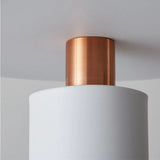 Close-up view of a pendant light fixture showing the junction of a cylindrical copper element and a larger matte white cylinder. The copper section displays a brushed finish, providing a warm metallic contrast to the smooth, stark white surface of the larger cylinder. The photograph emphasizes the clean lines and elegant simplicity of the design, suitable for modern interior aesthetics.